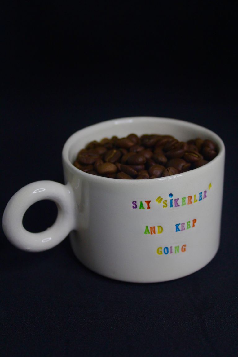 A white mug with colorful text filled with coffee beans against a black background.