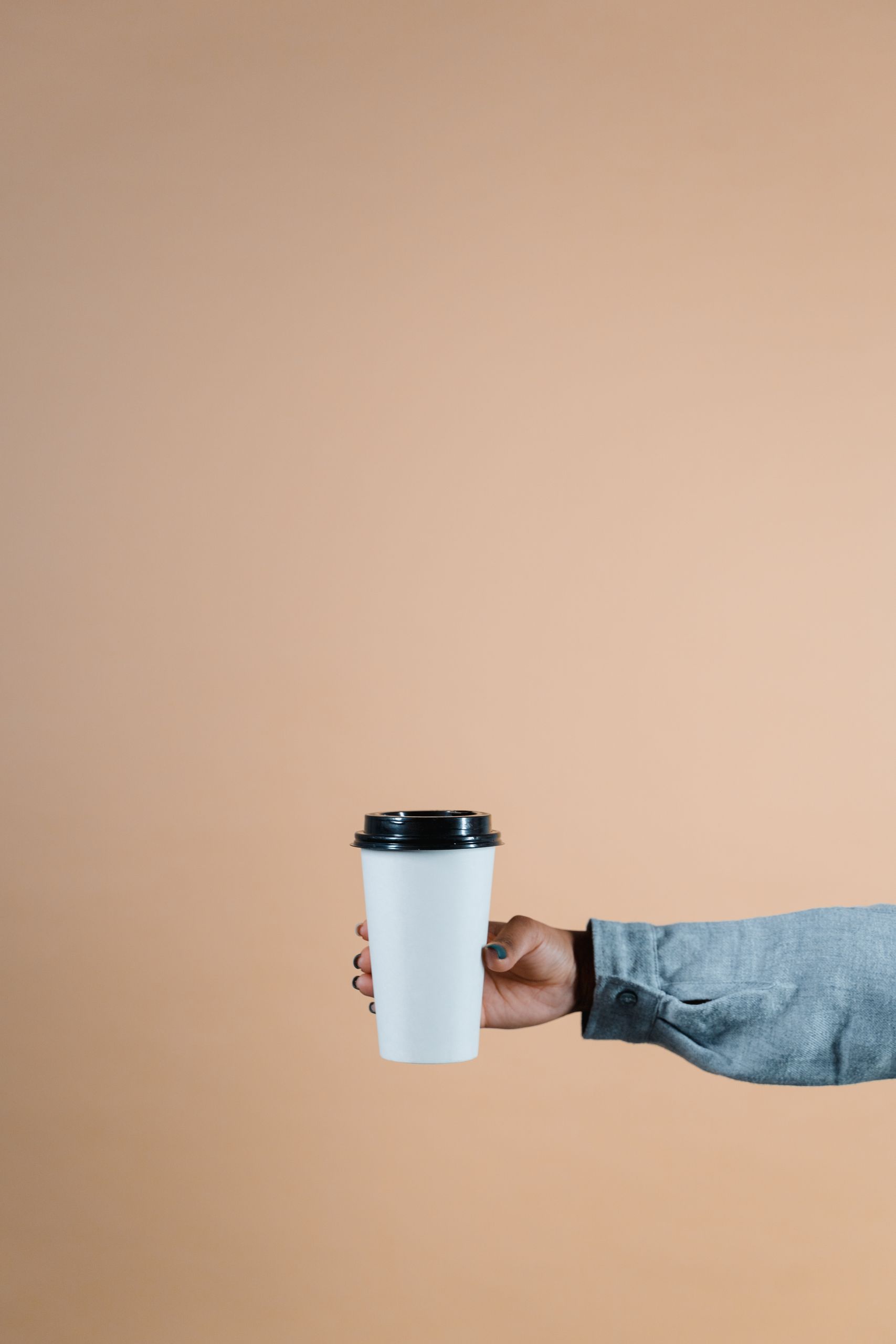 Person's hand holding a disposable coffee cup against a beige background.