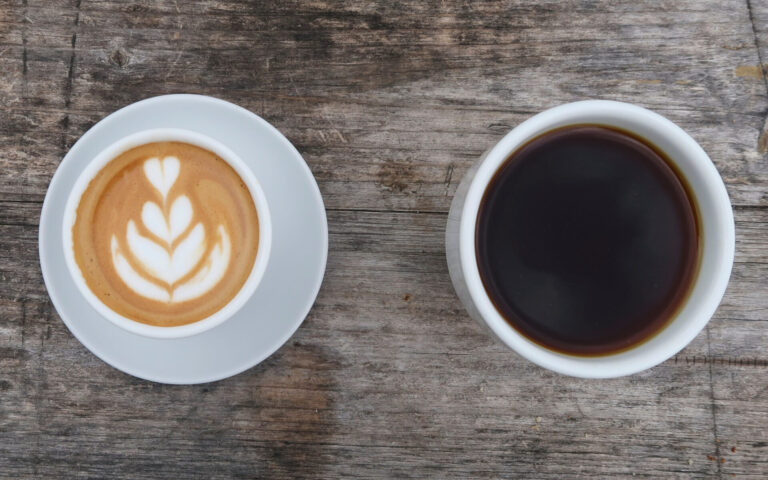 Overhead view of a latte and a black coffee in white cups, illustrating coffee choices for a protein latte