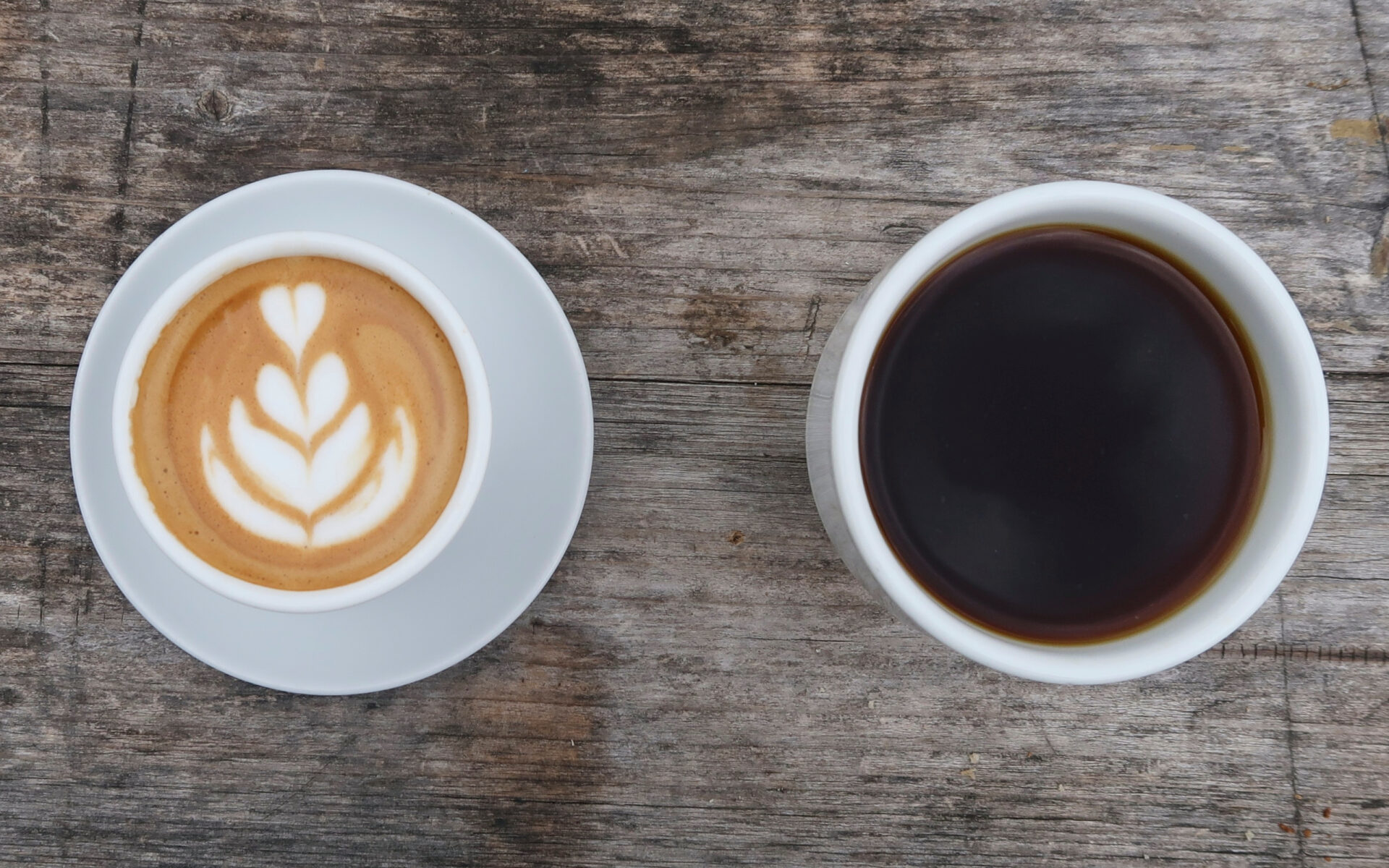 Overhead view of a latte and a black coffee in white cups, illustrating coffee choices for a protein latte